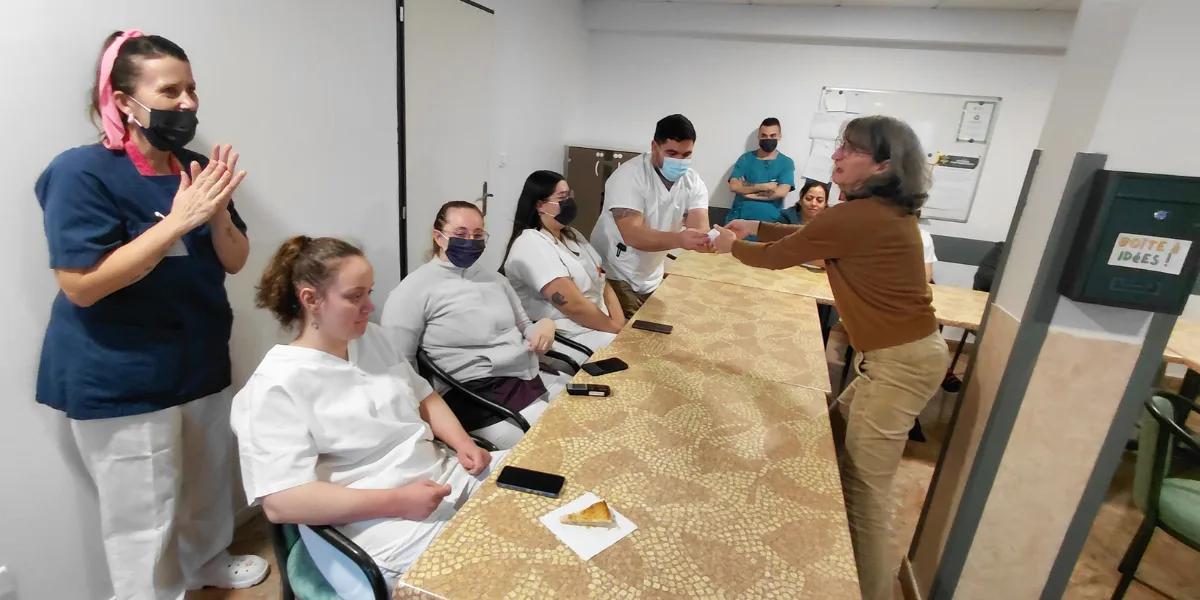 Groupe de personnes masquées autour d'une table, une femme debout applaudit à gauche